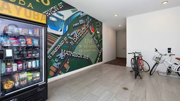 Máquina expendedora llena de bocadillos y un mural que muestra un paisaje urbano con una bicicleta.