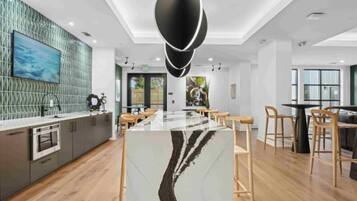 A modern kitchen with a marble island, wooden chairs, and a pendant light.