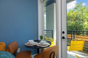 A balcony with a table set for two, chairs, and a view of a tree-lined street. - Loft  w/ King Bed, Balcony, Gym, Roof Top Terrace & Free Parking (Charlotte)