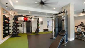 Uma academia com diversos equipamentos de exercício, um ventilador de teto e uma esteira.