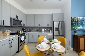A modern kitchen with grey cabinets, stainless steel appliances, and a dining area with yellow chairs and a glass table.