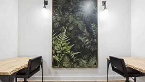 Uma sala de conferências com duas mesas de madeira, cadeiras pretas e um padrão de folha de samambaia grande na parede.