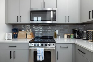 A modern kitchen with stainless steel appliances, grey cabinets, and a tiled backsplash. - 1BR King w/ Gym + Courtyard w/ Grill Station + Free Parking, NoDa Art District (Charlotte)