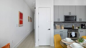 Cozinha moderna com armários cinza, micro-ondas e fogão. Há uma área de jantar com uma mesa posta para dois e uma cadeira amarela.