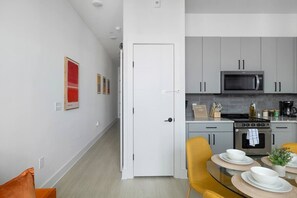 A modern kitchen with grey cabinets, a microwave, and a stove. There is a dining area with a table set for two and a yellow chair. - 1BR King w/ Gym + Courtyard w/ Grill Station + Free Parking, NoDa Art District (Charlotte)