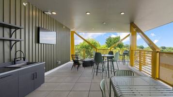 A modern outdoor dining area with a kitchen counter, chairs, and a TV mounted on the wall.