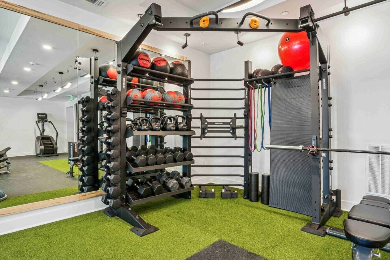 A gym with a mirrored wall, weight racks, kettlebells, and exercise equipment.