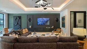 A modern living room with a sectional sofa, a flat-screen TV, and a unique ceiling light fixture.