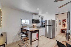 A modern kitchen with stainless steel appliances, a bar stool, and a window overlooking a cityscape. - Dual-Home Property with Private Patio (Henderson)