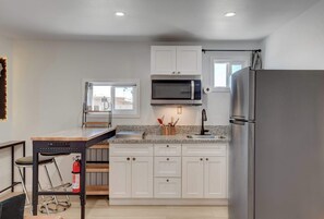 A modern kitchen with white cabinets, a stainless steel refrigerator, a microwave, and a window with a view. - Dual-Home Property with Private Patio (Henderson)
