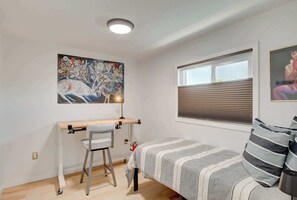 A bedroom with a desk, a chair, a bed with striped bedding, a window with blinds, and a ceiling light. - Dual-Home Property with Private Patio (Henderson)