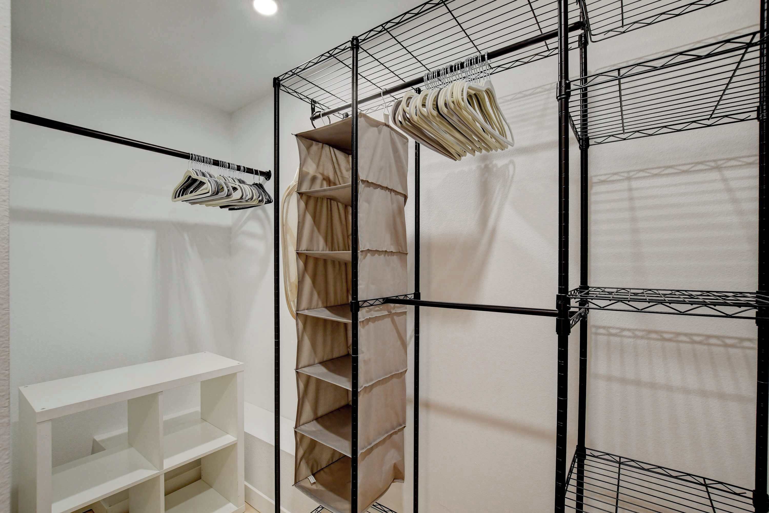 A room with a white shelving unit, a black metal rack with hanging items, and a beige curtain.