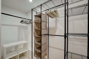 A room with a white shelving unit, a black metal rack with hanging items, and a beige curtain. - Dual-Home Property with Private Patio (Henderson)