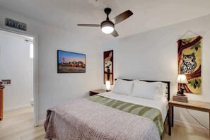 A hotel room with a bed, a nightstand, a lamp, a ceiling fan, and wall art. - Dual-Home Property with Private Patio (Henderson)
