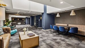 A modern hotel lobby with a checkered floor, seating areas, a reception desk, and a bar.