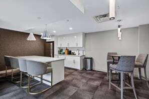 A modern kitchen with white cabinets, a stainless steel refrigerator, and a dining area with a table and chairs. - King Studio / Pool Table + Gym + Free Coffee Bar / 0.3 miles to Fountain Square (Cincinnati)
