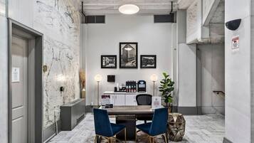 A hotel lobby with a marble wall, a reception desk, framed pictures, and a seating area with two chairs.