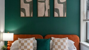 A bedroom with a teal wall, a bed with white and checkered pillows, and abstract art above the bed.
