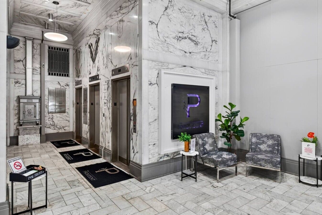 A lobby with marble walls, elevators, a reception desk, and a seating area with a plant.