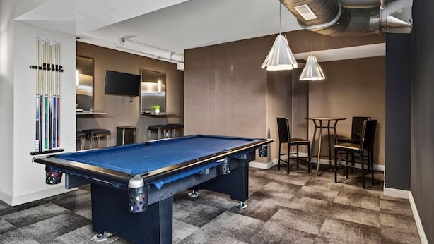 A pool table with chairs and a bar area in a modern room with a checkered floor.