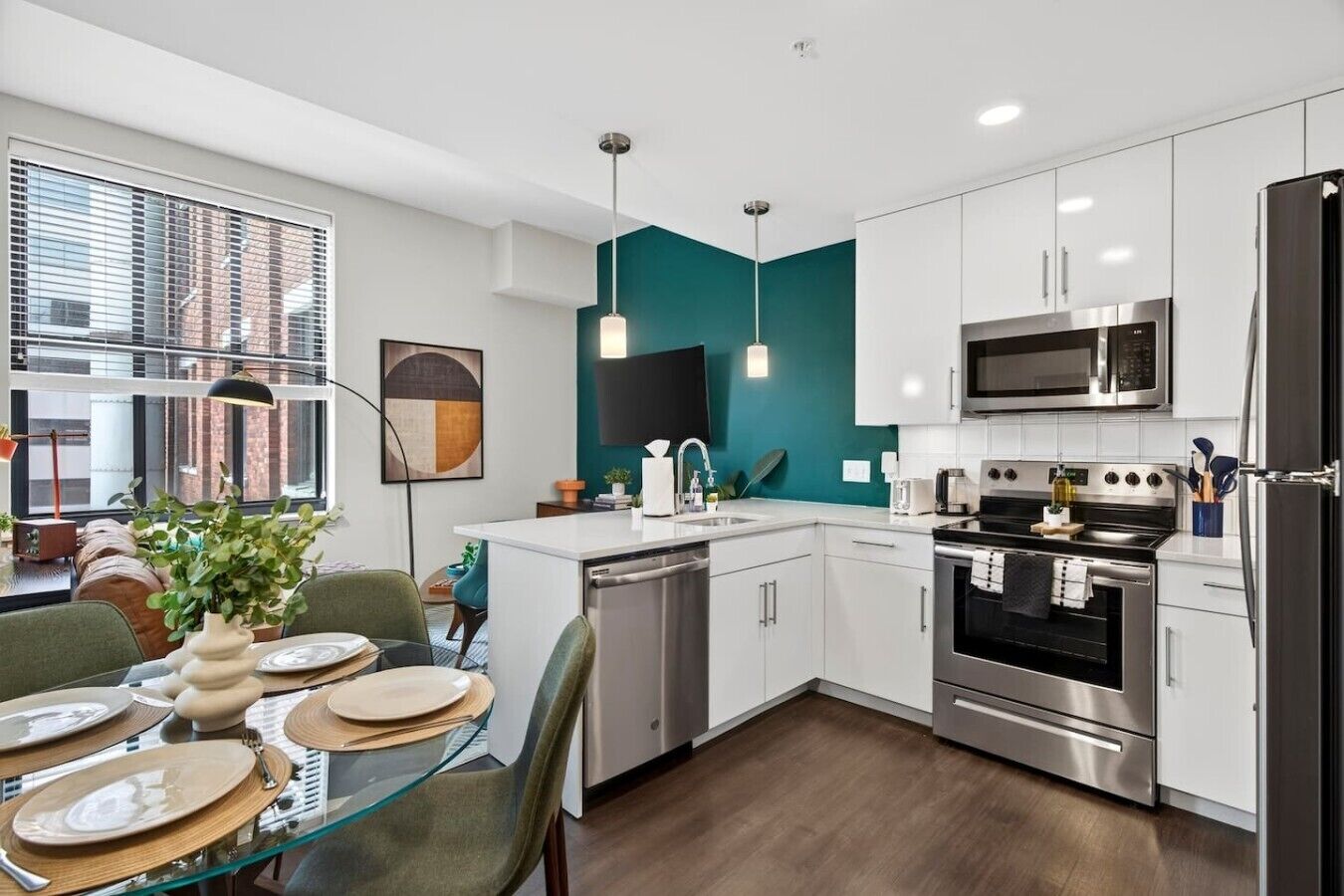 A modern kitchen with white cabinets, stainless steel appliances, and a teal accent wall.