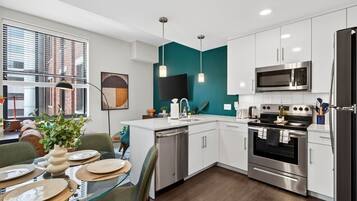 A modern kitchen with white cabinets, stainless steel appliances, and a teal accent wall.