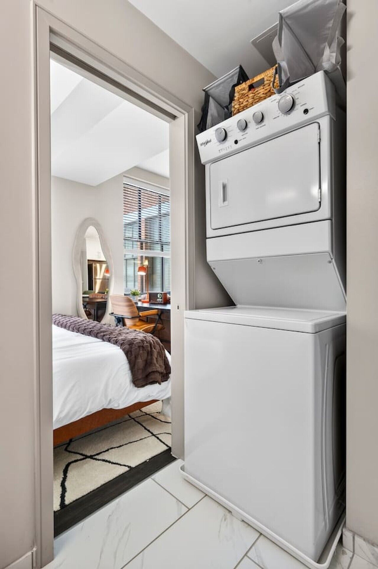 A compact hotel room with a bed, a small kitchenette with a stove, and a view of the city through the window.