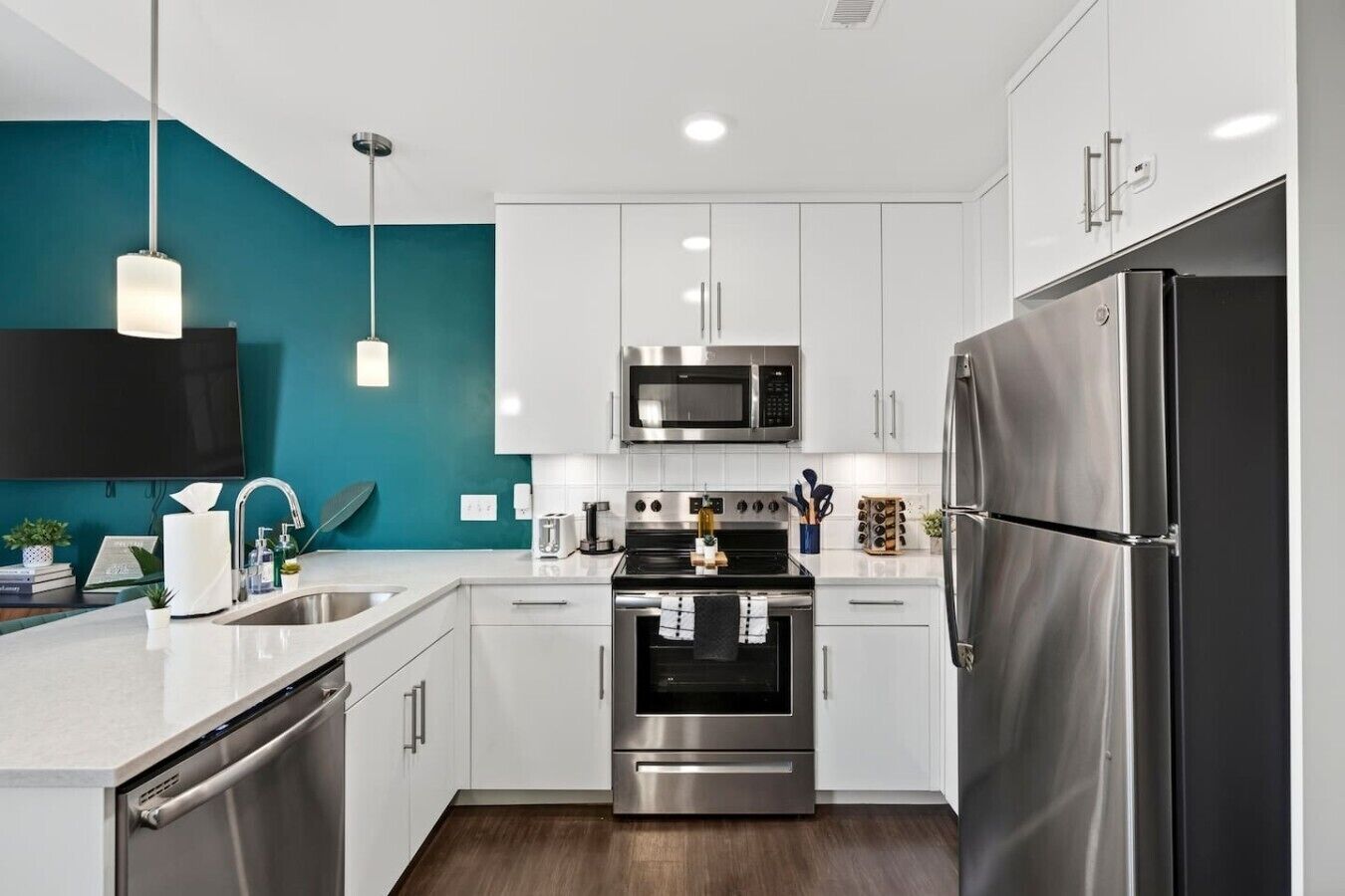 A modern kitchen with white cabinets, stainless steel appliances, and a teal accent wall.