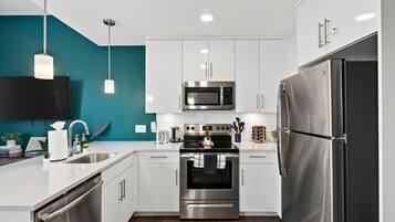 A modern kitchen with white cabinets, stainless steel appliances, and a teal accent wall.
