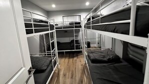Une chambre avec un lit superposé, un plancher en bois, des rampes blanches et une fenêtre avec des stores.