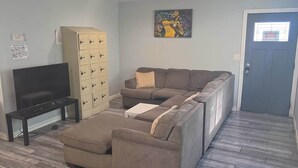Un salon comprenant un canapé, un pouf, un téléviseur et des rangements.