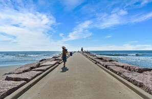 A concrete walkway leading to the beach with a person walking away from the camera. - Cozy Family Home with Game Room, Near Downtown (Galveston)