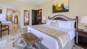 Une chambre d’hôtel avec un grand lit, un coin salon avec un banc, une salle de bain avec une baignoire et un tableau au mur.