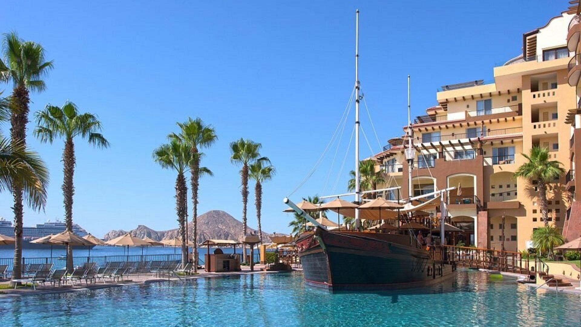 Une piscine avec un bateau, des palmiers et un bâtiment d’hôtel.