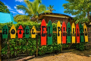 Una valla de madera con letreros con forma de tabla de surf de colores que deletrean 'HOTEL EL PARADISO'.