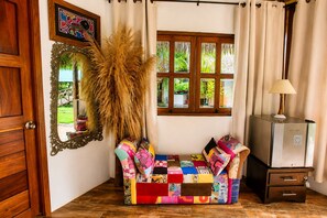 A room with a wooden door, a mirror, a colorful sofa, a lamp, and a radiator. - Hotel Cabañas el Paraiso en Sapzurro (Sapzurro)