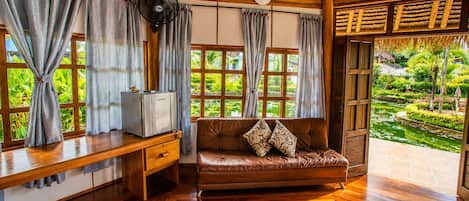 Una habitación con techo de madera, un sofá con cojines estampados, un escritorio de madera con televisor y ventanas grandes con cortinas.