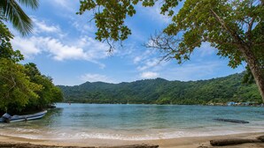 A beach with a boat, calm water, and a forested hillside.