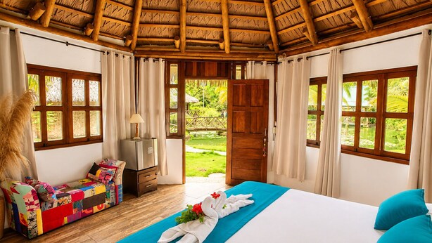 A room with a bed, a sofa, a lamp, and a view of a garden.