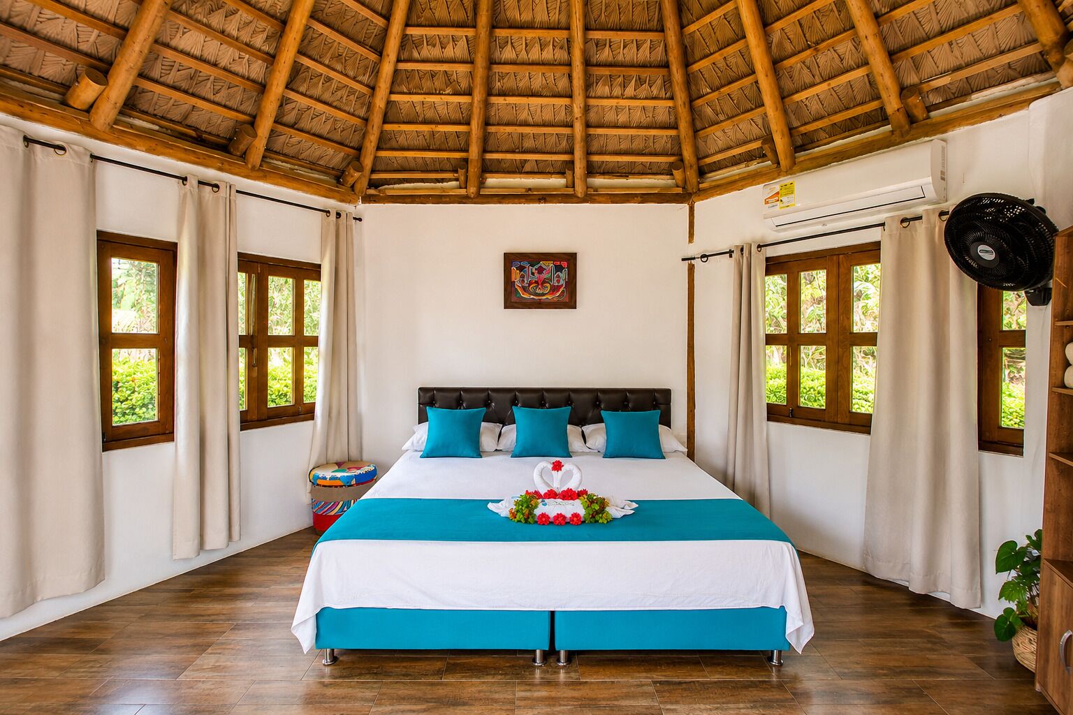 A hotel room with a bed, a window, a ceiling fan, and a wall-mounted air conditioner.