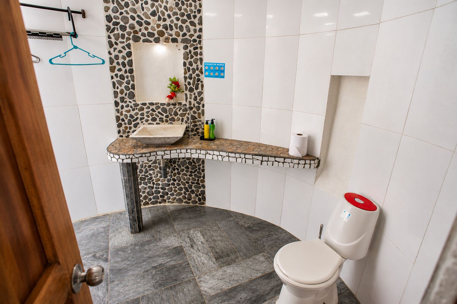 A bathroom with a stone mosaic backsplash, a sink with a countertop, a toilet, and a shower area.