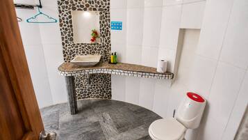 A bathroom with a stone mosaic backsplash, a sink with a countertop, a toilet, and a shower area.
