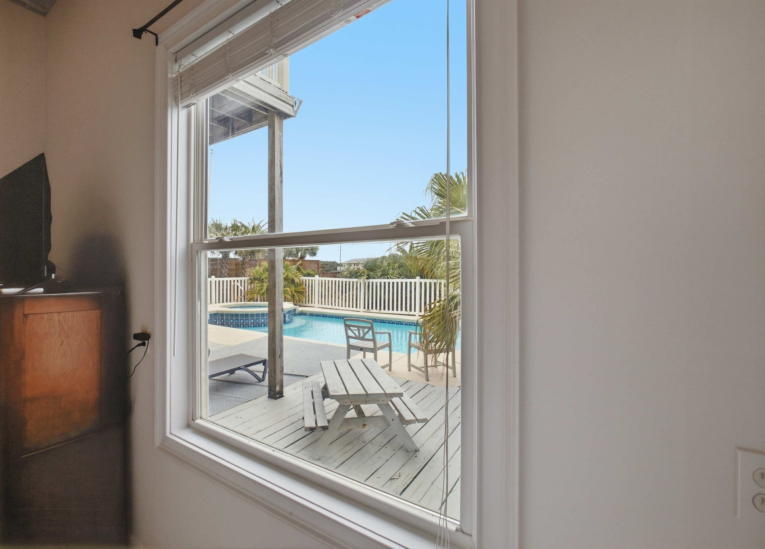 Une fenêtre donnant sur une piscine et sur du mobilier d’extérieur.