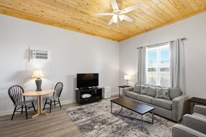 Ein Wohnzimmer mit Deckenventilator, Fernseher, Sofa, Couchtisch und einem Essbereich mit Stühlen.