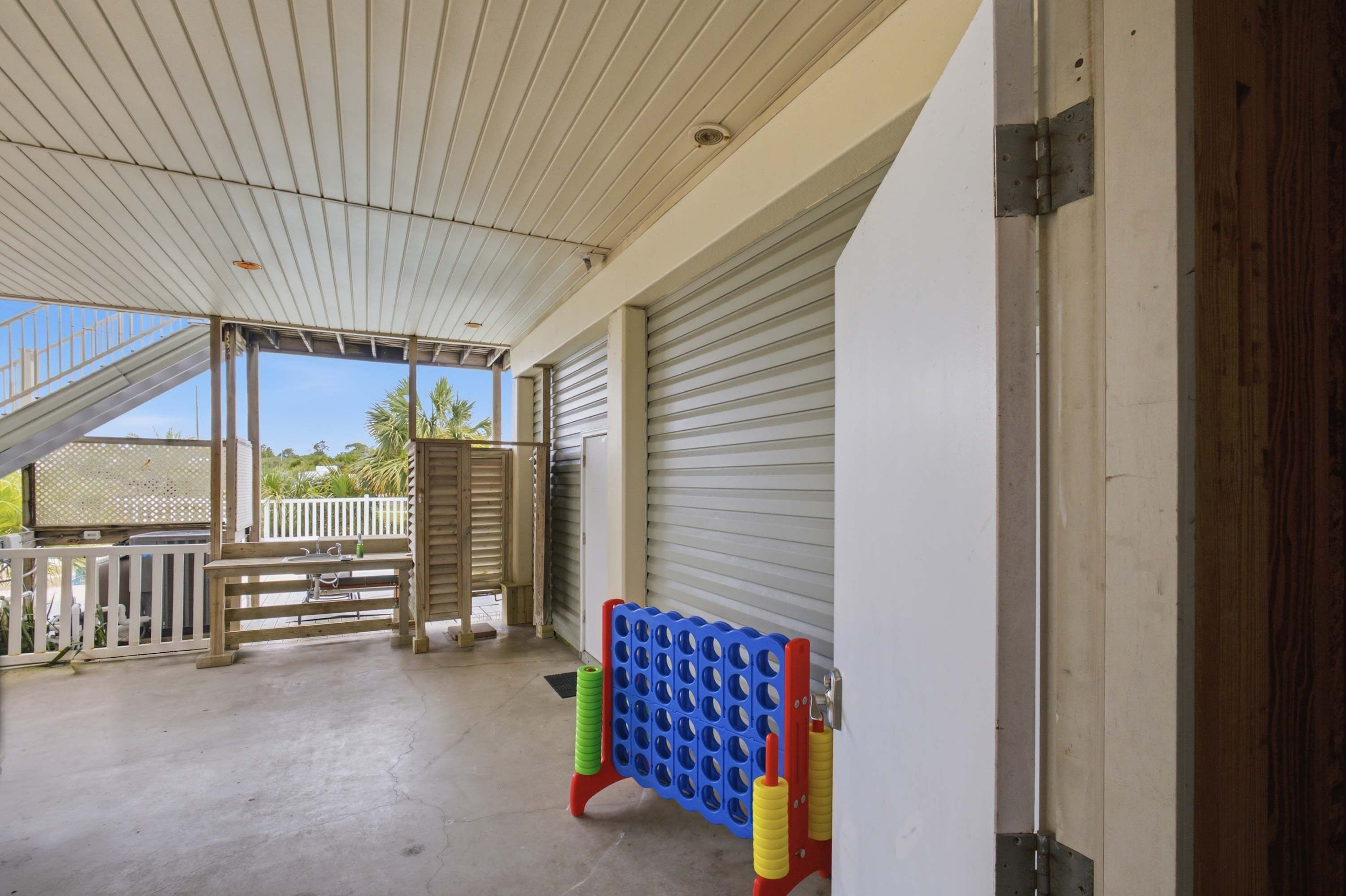 Un espace extérieur abrité doté d’un sol en béton, d’un banc en bois, d’une structure de jeu bleue et rouge, et d’une porte de garage fermée.
