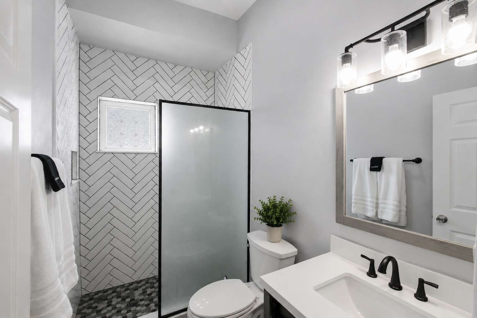 Une salle de bain moderne avec une douche à parois de verre, des toilettes blanches, un lavabo avec des robinets noirs et un miroir avec éclairage intégré.