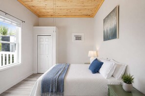 Ein Schlafzimmer mit Bett, Nachttisch, Lampe, Fenster und Tür.