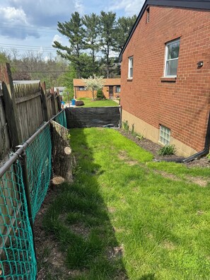 A residential backyard with a brick house, a wooden fence, and a green lawn. - 3-bedroom house in welcoming Pittsburgh with cool AC breeze (Pittsburgh)