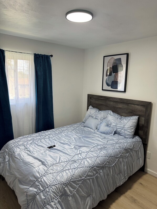 A bedroom with a bed, a ceiling light, a window with curtains, and a framed picture on the wall.