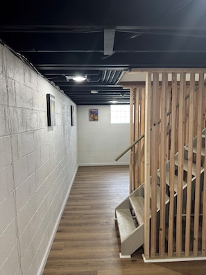Un pasillo estrecho con una escalera de madera a la derecha, paredes de ladrillo blanco y un ventanal al final.
